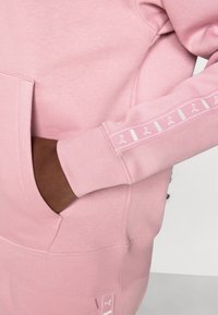 Lys rosa gensere laget av myk stoff, med kengurulomme, ribbede mansjetter og et logo-trykket accent på ermet.