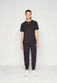 T-shirt e calças atléticas pretas feitas de tecido respirável, com um design simples. Os sapatos são brancos com um estilo minimalista.