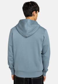 Felpa con cappuccio azzurro chiaro realizzata in tessuto morbido, con cappuccio regolabile tramite cordino, polsini e vita a costine, dal taglio comodo e con dettagli minimi.