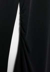 Priblizek črne tkanine z zbranimi detajli, ki ustvarjajo navpične gube, na sredini pa kontrastno belo ozadje.