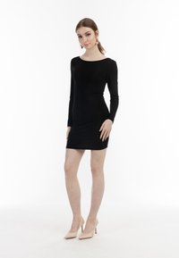 Schwarzes, tailliertes Langarmkleid mit Rundhalsausschnitt. Glatte Textur, knielang, kombiniert mit hautfarbenen High Heels. Schlichtes Design.