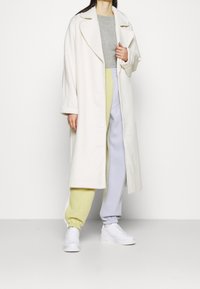 Vit oversized kappa, grå tajt topp, pastellfärgade byxor i grönt och lavendel, tillsammans med vita sneakers. Mjuka material och avslappnad passform.