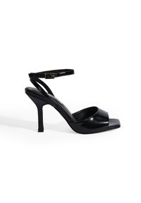 Zwarte gepatineerde leren hoge hak sandalen met een vierkante neus, enkelsluiting en een slanke hak. Glad textuur met een glanzende afwerking.