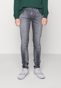 Jeans de corte slim, en gris desgastado con un ligero desgaste, diseño de cinco bolsillos, cierre de botón metálico, costuras cosidas, combinados con zapatillas blancas.