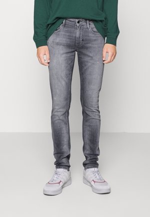 Jeans de corte slim, en gris desgastado con un ligero desgaste, diseño de cinco bolsillos, cierre de botón metálico, costuras cosidas, combinados con zapatillas blancas.