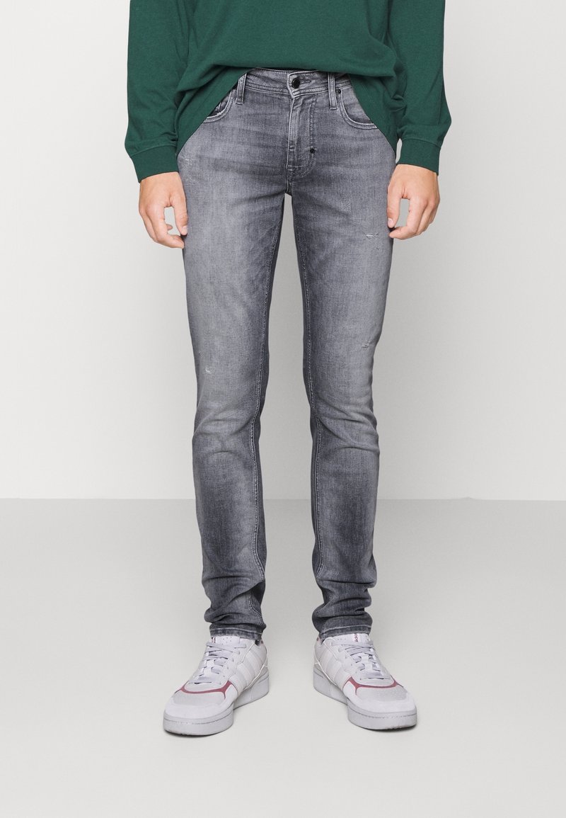 Jeans de corte slim, en gris desgastado con un ligero desgaste, diseño de cinco bolsillos, cierre de botón metálico, costuras cosidas, combinados con zapatillas blancas.