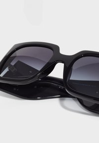 Gafas de sol rectangulares negras con lentes oscuros en degradado. La montura es de plástico brillante, con un diseño ancho y bordes suaves.