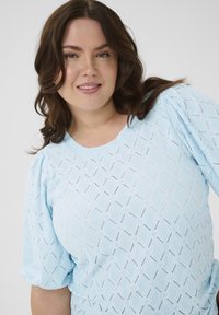 Light blue blouse featuring a textured diamond pattern, short puff sleeves, and a round neckline for a comfortable fit.