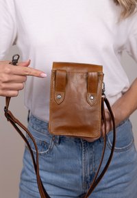 Brun läder crossbody-väska med rektangulär form, metalltryckknappar och en strukturerad yta; har justerbar axelrem.