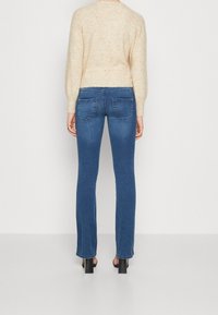 Niebieskie wąskie jeansy z dyskretnymi tylnymi kieszeniami, z średnim stanem i czystym dołem. Połączone z jasnym, teksturowanym swetrem w kolorze kremowym.