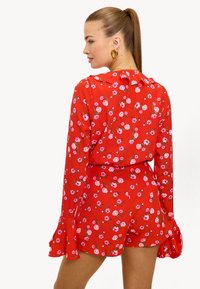 Mono rojo con flores, de manga larga acampanada y escote con volantes. El patrón presenta flores rosas y verdes sobre una tela ligera y suave.