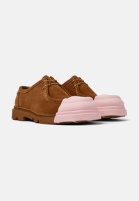 Scarpe in suede marrone con lacci e punte rinforzate in gomma rosa spessa su uno sfondo bianco.