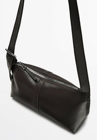 Borsa a tracolla in pelle nera con apertura con zip, forma rettangolare, base piatta e tracolla regolabile con fori per la regolazione della lunghezza.