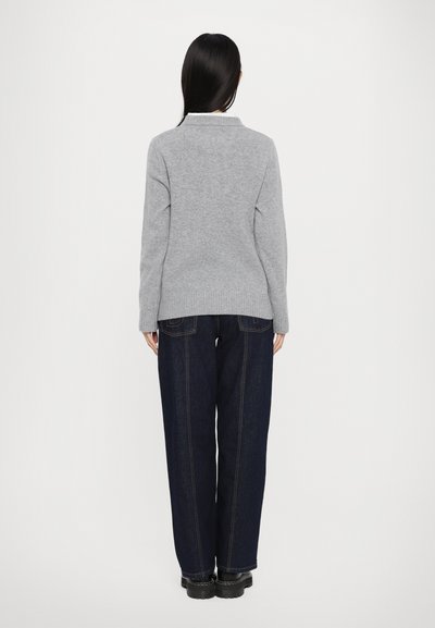 Maglione grigio a maglia con colletto a costine, abbinato a pantaloni di jeans blu scuro a vita alta. L'outfit ha un fit rilassato e dettagli minimi.