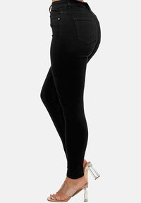 Jeans skinny negros de denim con una textura suave, que cuentan con una cintura alta, cinco bolsillos y detalles de desgaste ligero. Sandalias de tacón transparente.