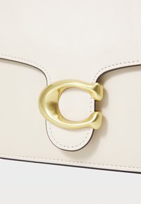 Cream leather handbag featuring a gold metal clasp, contrasting stitching, and a rectangular shape. Smooth texture with rounded edges.