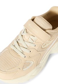 Sneaker beige Champion con upper in mesh e pelle, fascia in velcro, lacci in tessuto e suola ammortizzata, mostrata da un angolo frontale superiore.