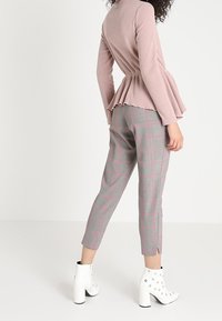 Rosa gerippter Peplum-Top mit langen Ärmeln; graue karierte tapered Hose mit rosa Akzenten; weiße Stiefeletten mit Absatz und runden Nieten.