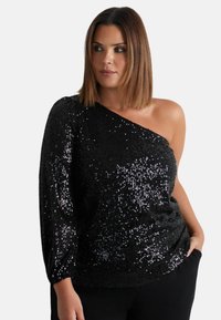 Top nero con paillettes, design a spalla scoprente, caratterizzato da una vestibilità ampia e una texture arricciata. Tessuto liscio con paillettes lucide che riflettono la luce.