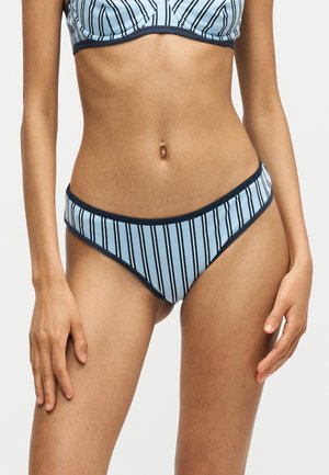 Kvinde model iført lyseblå bikiniunderdel og -top med lodrette sorte striber og mørk kant på ensfarvet baggrund.