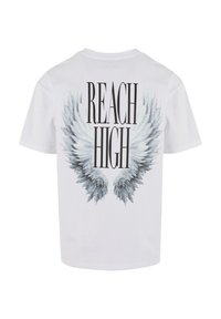 T-shirt en coton blanc avec un grand graphique d'aile grise et le texte "REACH HIGH" en lettres noires en gras au dos.