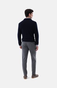Marineblauen Pullover mit strukturiertem Finish, graue Karohosen und braune Wildleder-Ankle Boots. Sichtbare Hemdmanschetten unter dem Pullover.