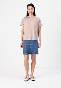 Lys beige kortermet t-skjorte kombinert med et blått denimskjørt med frontknapper og lommer; brukt med lyse flate sko.