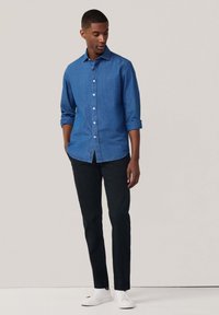 Lichtblauwe denim overhemd met knopen, opgerolde mouwen, klassieke kraag, gecombineerd met zwarte chino's en witte sneakers, zonder zichtbare logo's.