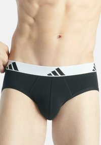 Zwarte slip met witte elastische tailleband met drie zwarte strepen. Gemaakt van gladde stof met gestikte details.