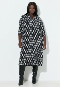 Długi płaszcz w czarno-białe wzory, z kołnierzem, trzy czwarte rękawami i zapięciem na guziki. Miękki materiał z geometrycznym wzorem kół.