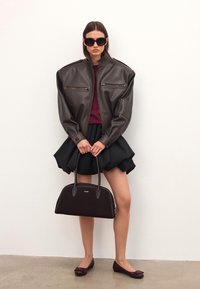 Smeđa kožna oversized jakna s patentnim zatvaračima, bordo pulover, crna suknja s voluminoznim krojem, smeđa torba i tamne balerinke.