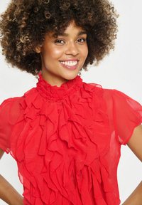 Rote Chiffonbluse mit hohem Rüschensaum, kurzen Ärmeln und einem strukturierten, mehrlagigen Design mit Knopfverschluss an der Vorderseite.