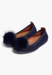 Des ballerines en daim bleu marine avec une semelle flexible, arborant deux grands pompons en fourrure sur les orteils et un intérieur lisse.