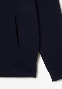 Manche et poche de sweat-shirt bleu marine foncé avec poignets et ceinture côtelés sur fond blanc.