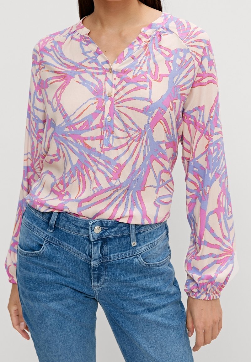 Blouse colorée en rose clair avec des motifs abstraits bleus et violets, dotée d'un col en V, d'une patte de boutonnage et de manches longues froncées.