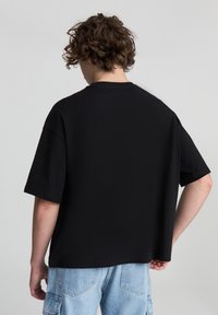 T-shirt nera ampia con maniche corte, colletto rotondo e materiale in cotone morbido. Cuciture visibili e orlo dritto sul fondo.