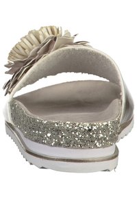 Bakvy av en sandal med en glittrig silverfärgad sula, beige plyschrem och dekorativ blomma. Slät yta och öppen design.
