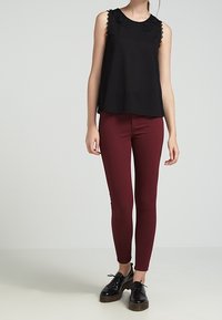 Černý bezramínkový top s texturovaným krajkovým výstřihem, zkombinovaný s burgundskými legínami a černými platformovými botami, stojící na neutrálním pozadí.