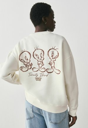 Person trägt weißen Pullover mit drei Skizzen von Tweety Bird und dem Schriftzug „Tweety Bird Looney Tunes“ auf der Rückseite.