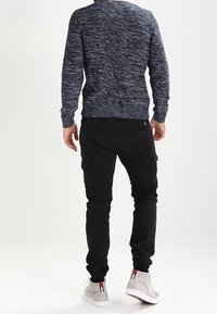 Pull en tricot texturé bleu marine avec poignets côtelés, associé à un pantalon cargo noir avec poches, et des baskets montantes grises.