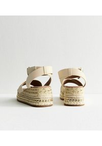 Beige espadrillosandaler med ankelsnören, plattformssula av jute, texturerad vävd detalj och metalliska accenter ovanför sulan.
