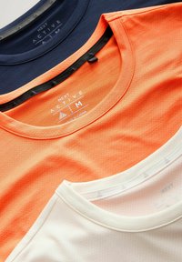 Drei gefaltete Next Active Crewneck-Sportshirts in Marineblau, Orange und Weiß, Größe Medium, aus atmungsaktivem Stoff.
