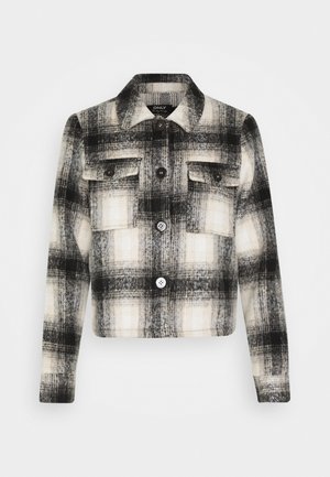 Veste à manches longues à carreaux noir et blanc avec col, devant à boutons et deux poches poitrine à boutons sur un fond uni.