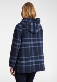Abrigo de cuadros azul marino con capucha, que presenta un patrón de cuadros azules, un corte holgado y mangas hasta el codo, fabricado en una tela suave y texturizada.