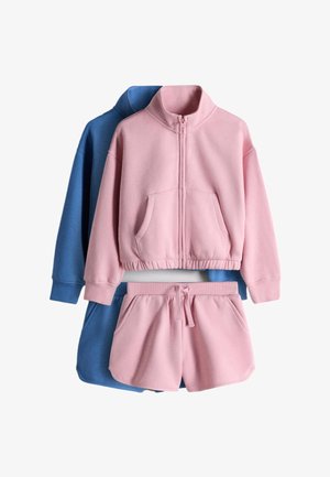 Pink sweatshirt med lynlås og shorts sat lagdelt over en blå sweatshirt og shorts på hvid baggrund.