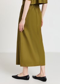 Gonna maxi verde oliva con vita elastica e texture liscia, abbinata a scarpe basse nere. Vista posteriore che mostra la lunghezza e la vestibilità della gonna.