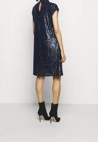 Navy sequin dress with cap sleeves, back keyhole detail, and loose fit, paired with black ankle boots featuring high heels and pointed toes.