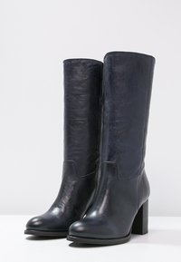 Bottes en cuir bleu marine montant jusqu'aux genoux, avec une texture lisse, un bout arrondi, un talon bloc, et une discrète couture à l'avant.