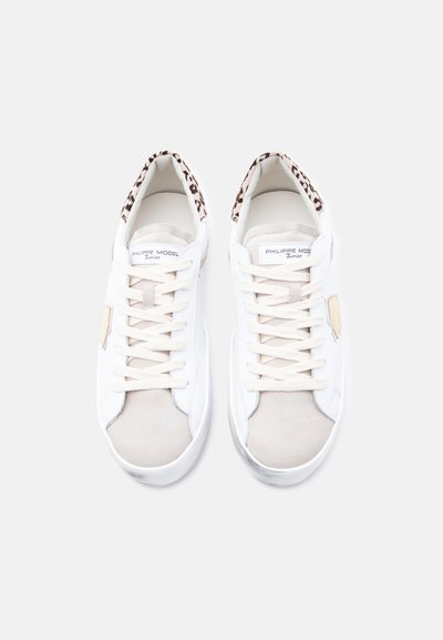 Baskets blanches avec un embout en daim et un intérieur imprimé léopard, présentant des accents beige et des lacets plats. Logo signature sur la languette.