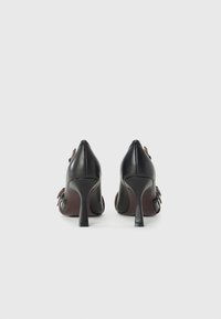 Chaussures à talons hauts en cuir noir avec un bout pointu, présentant un design arrière élégant et un talon mince pour plus de stabilité.